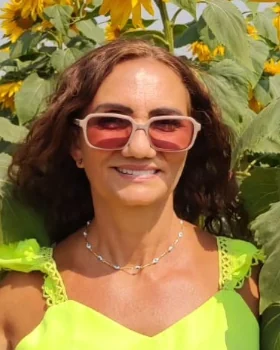 Francy Martins sorrindo, de óculos, entre girassóis.